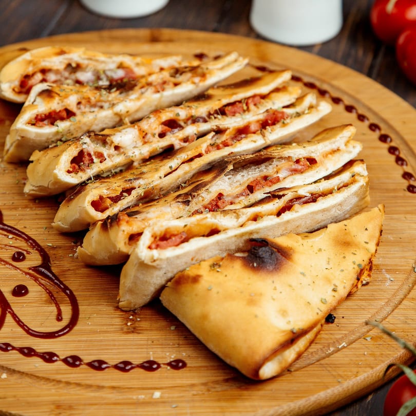 Sliced calzones with cheese and pepperoni on a wooden board, garnished with sauce and herbs.