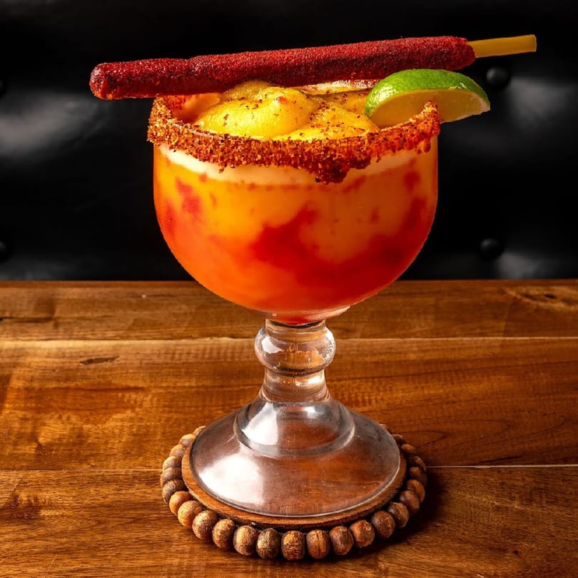 A vibrant Condesa Tacos & Tequila mangonada with a chili straw, lime, and chili-salted rim.