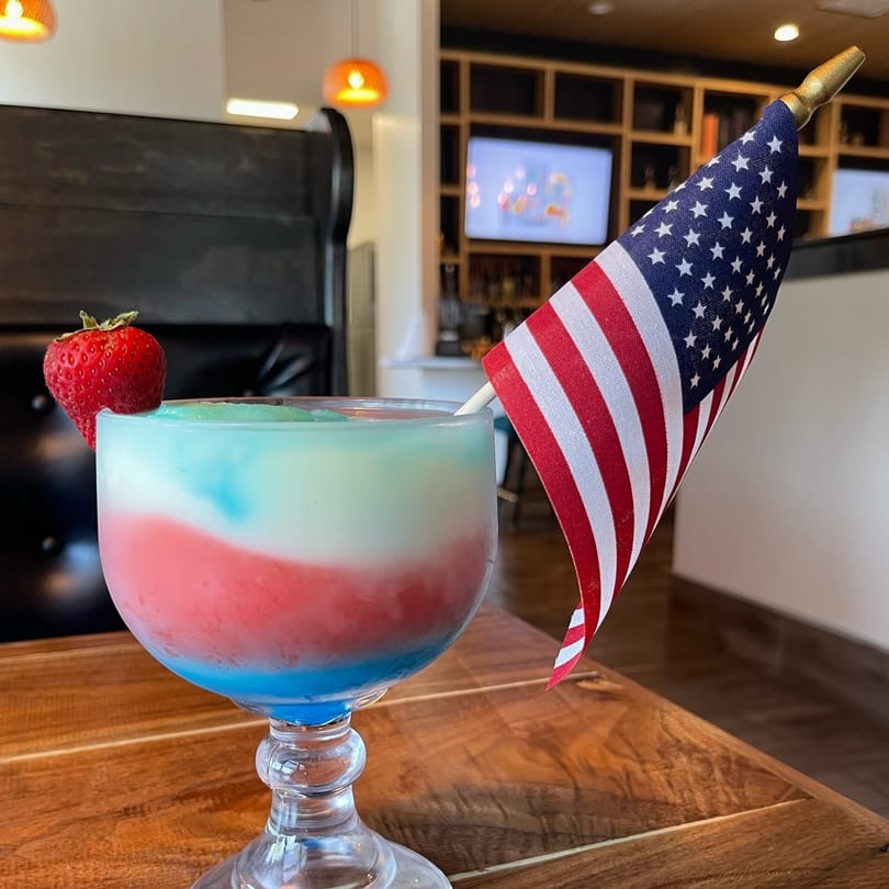 Red, white, and blue frozen drink with a strawberry and American flag on a wooden table.