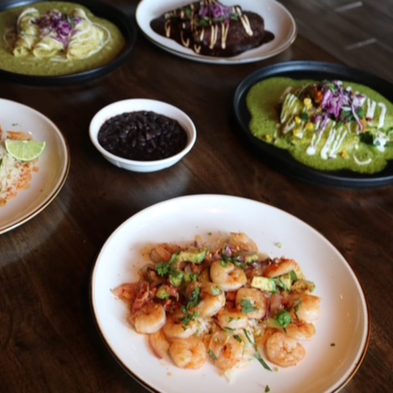 A table spread with various Mexican dishes, including shrimp, enchiladas, and black beans.