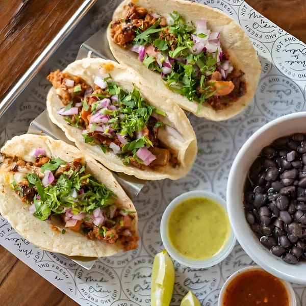 Three Condesa Tacos with meat, cilantro, and red onions, served with black beans and sauces.