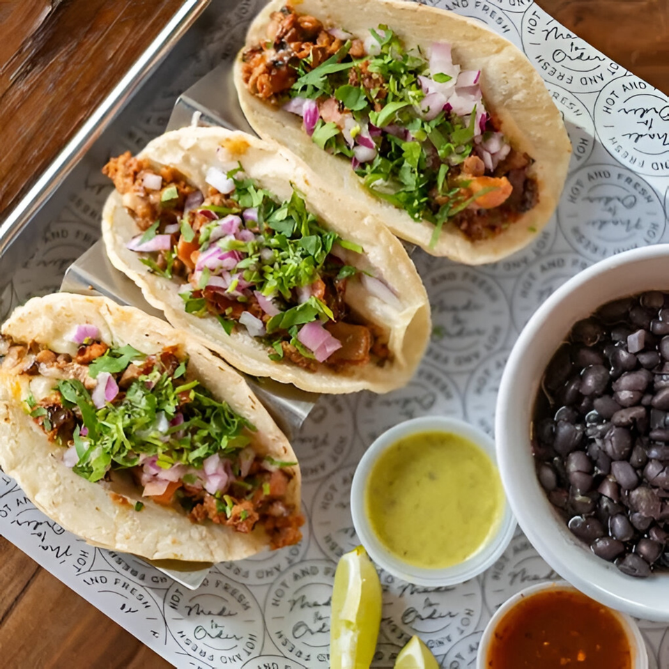 Three Condesa Tacos with meat, cilantro, and red onions, served with black beans and sauces.