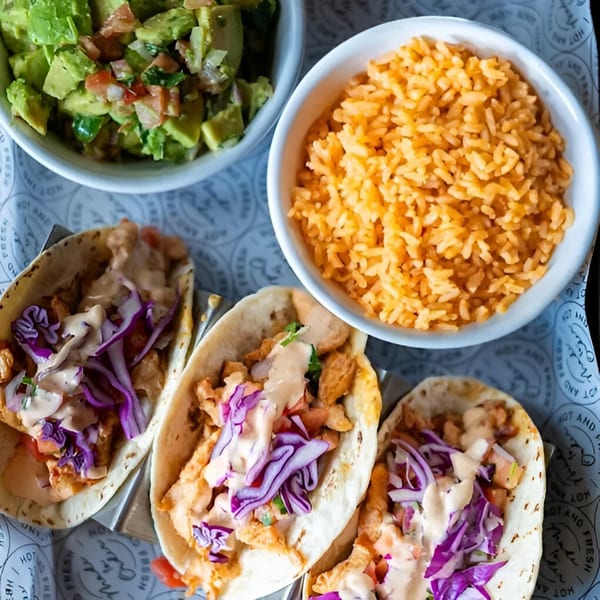 Three Condesa Tacos with red cabbage, sauce, and chicken, served with rice and guacamole.