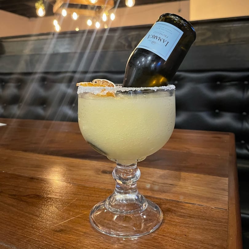 A large frozen margarita with a La Marca Prosecco bottle inverted into it, garnished with dried orange slices.