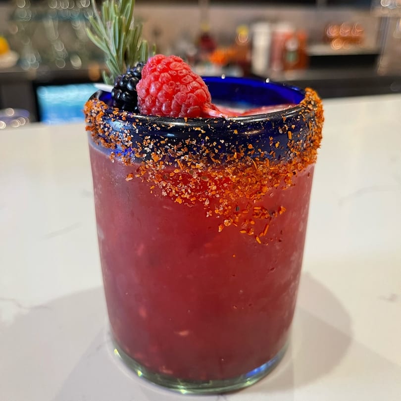 Condesa Tacos & Tequila's red cocktail with a chili-salt rim, garnished with a raspberry, blackberry, and rosemary.